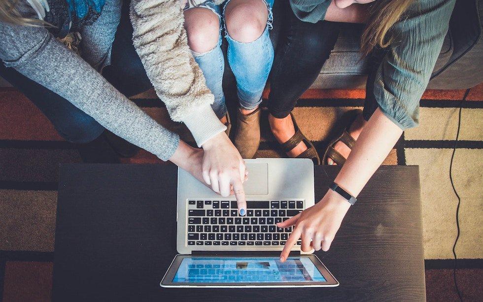 Three people pointing at a laptop screen, likely collaborating or discussing something on the screen.