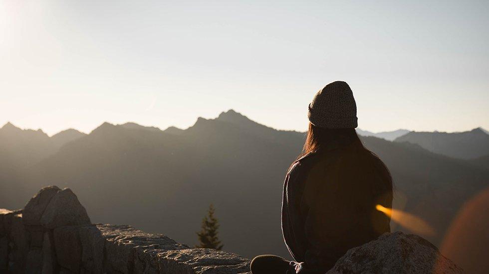 Person wearing knit cap facing mountain range